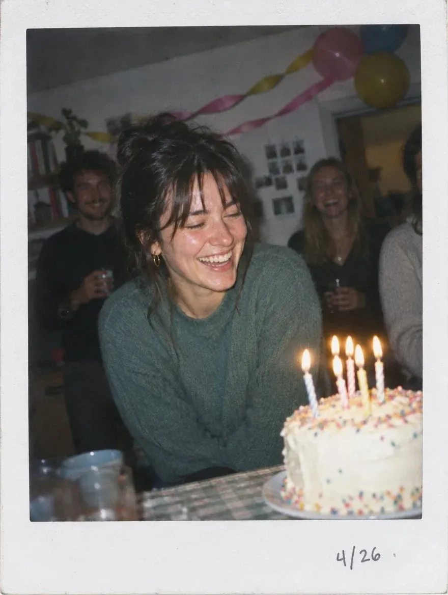 A woman joyfully smiles at a birthday cake with candles.