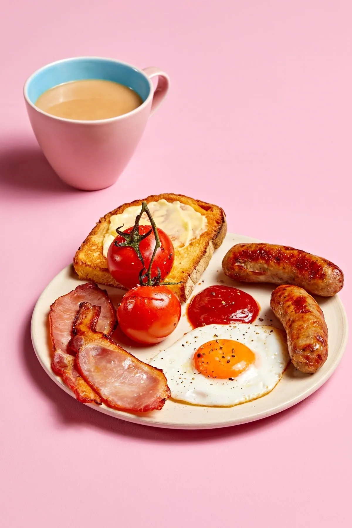 Un piatto per la colazione con uova, pancetta, salsicce, pomodori e una tazza di caffè.