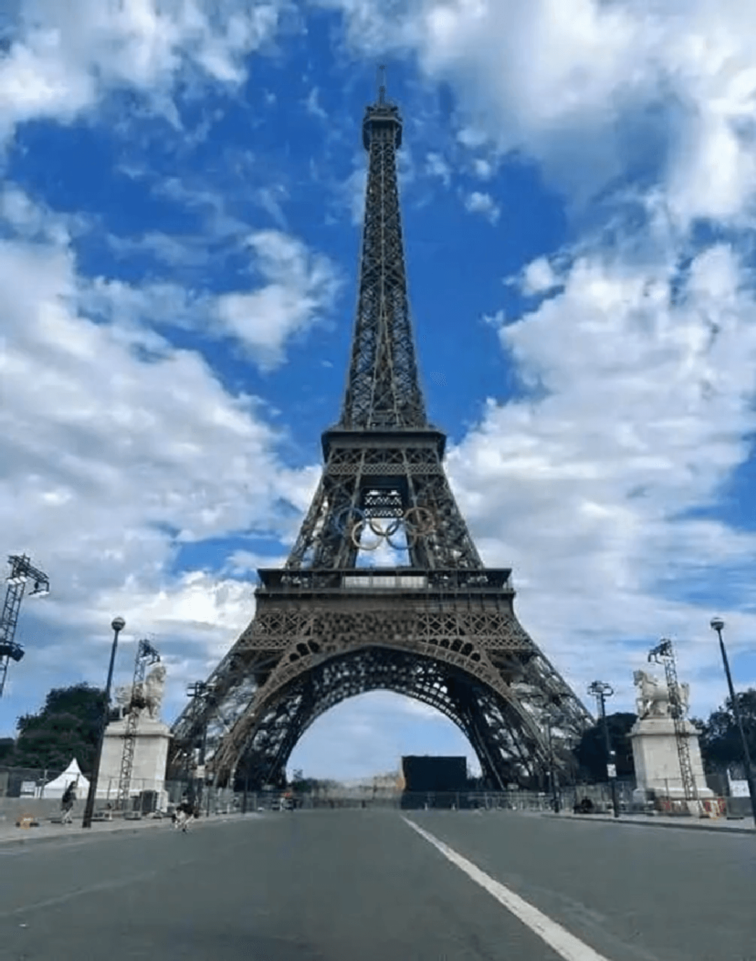 Vista gran angular de la Torre Eiffel en París bajo un cielo azul con nubes dispersas.