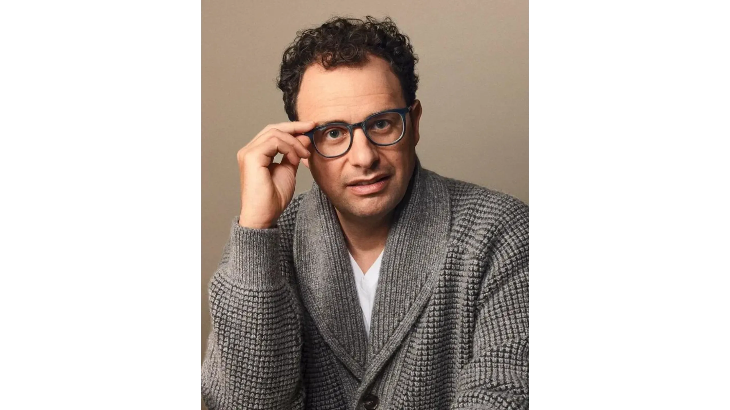 A man wearing glasses and a gray sweater poses thoughtfully.