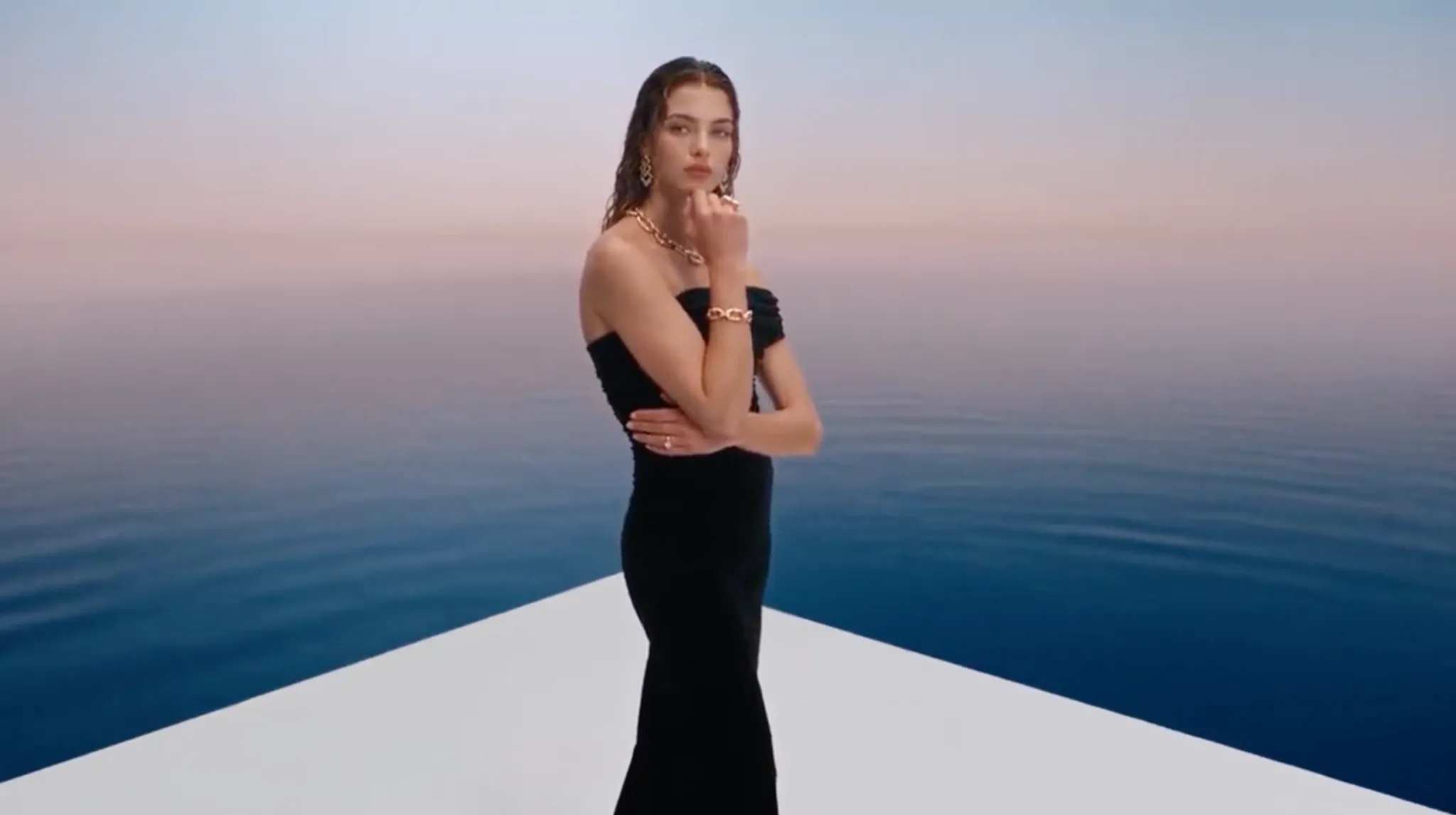 Een model poseert in een zwarte jurk tegen een serene waterachtergrond.