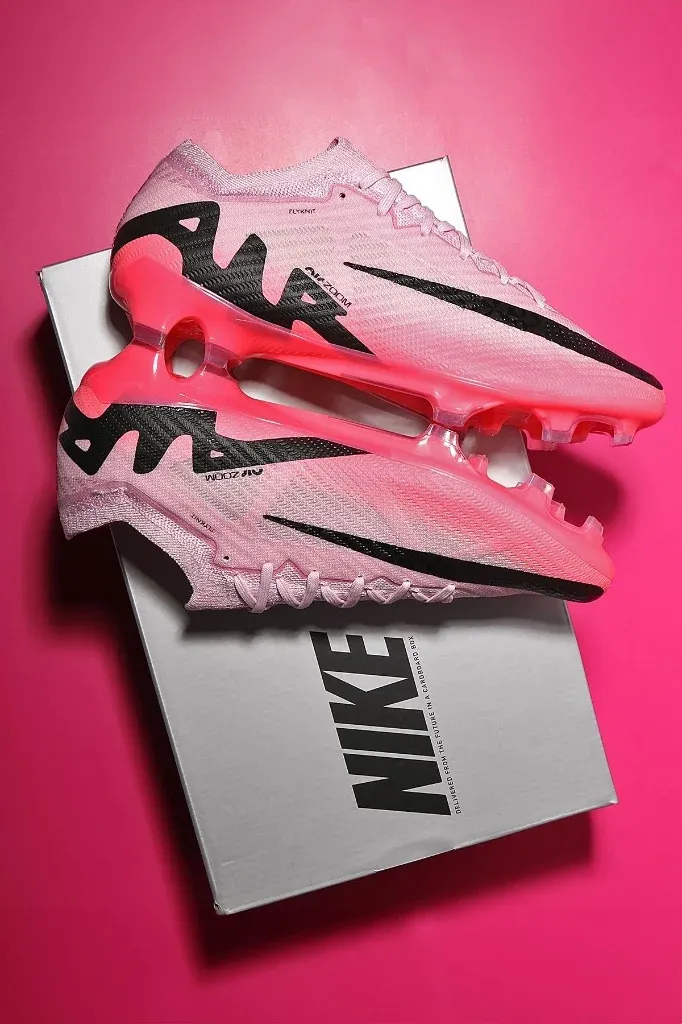 A pair of pink Nike soccer cleats on a gray box against a pink background.