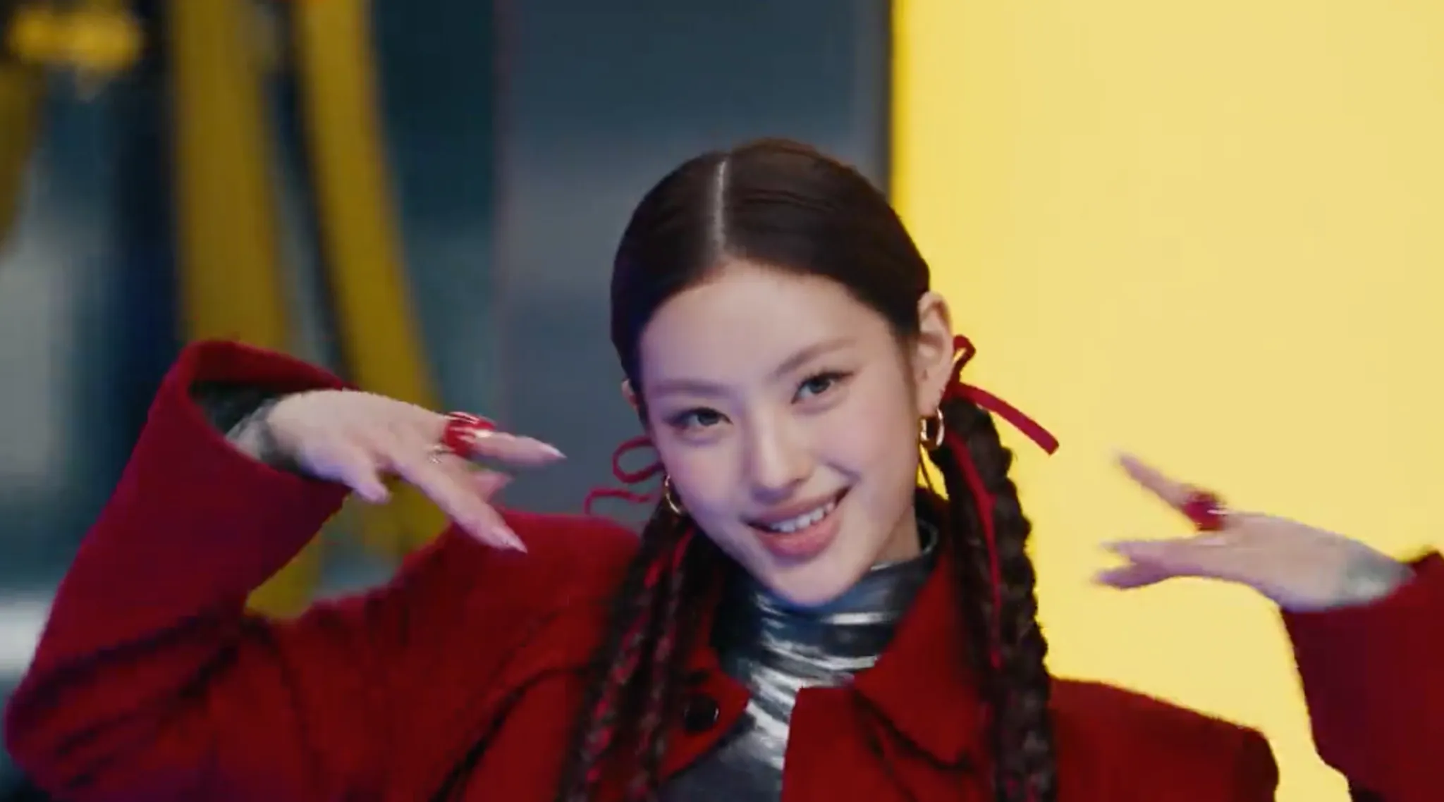 A woman with braided hair smiles and poses in a red coat against a colorful background.