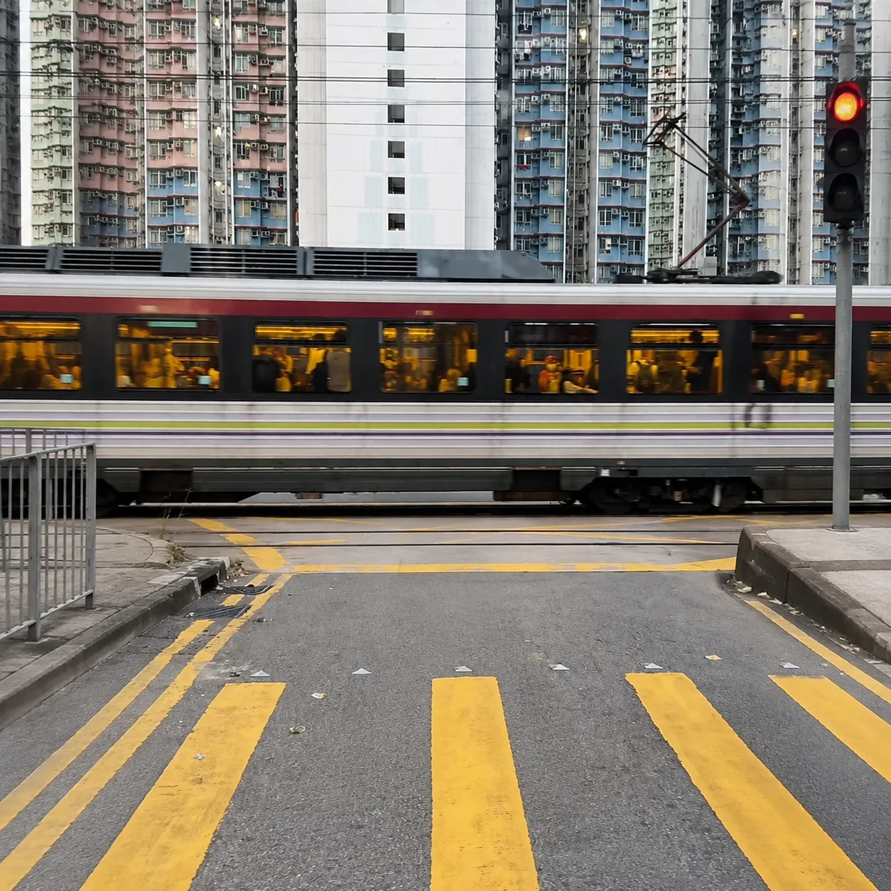 A train passes by a crosswalk in a busy urban setting with high-rise buildings.