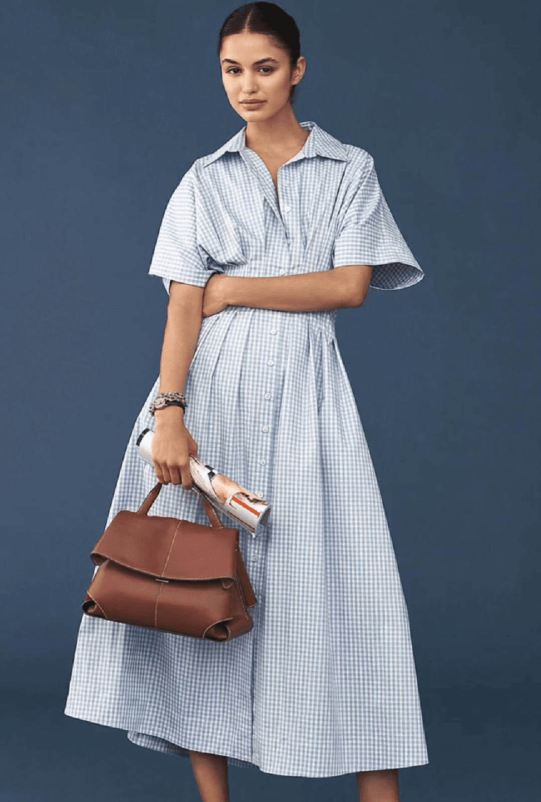 Una mujer con un vestido de cuadros azules y un bolso de mano marrón.
