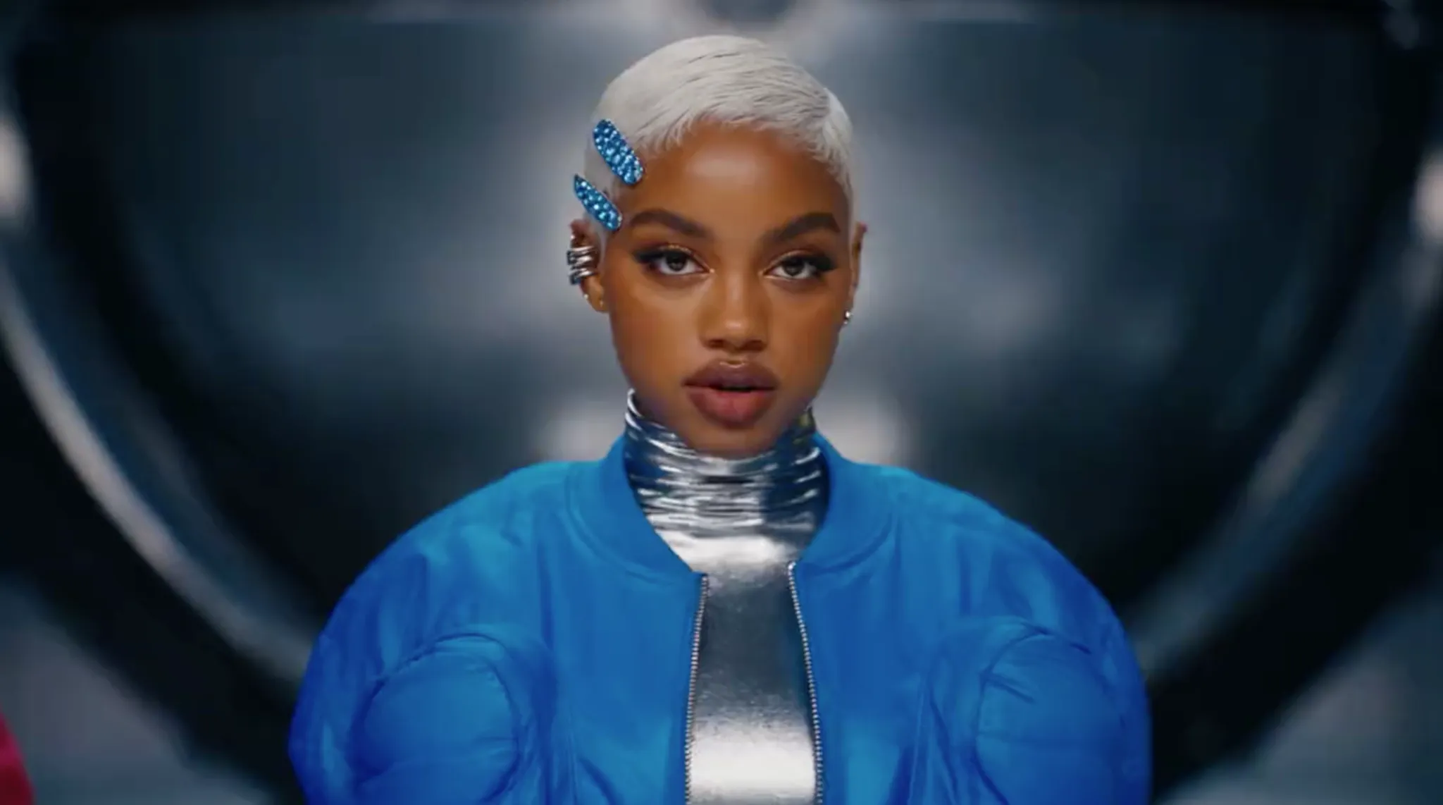 A woman with short platinum hair wears a blue jacket and silver collar.