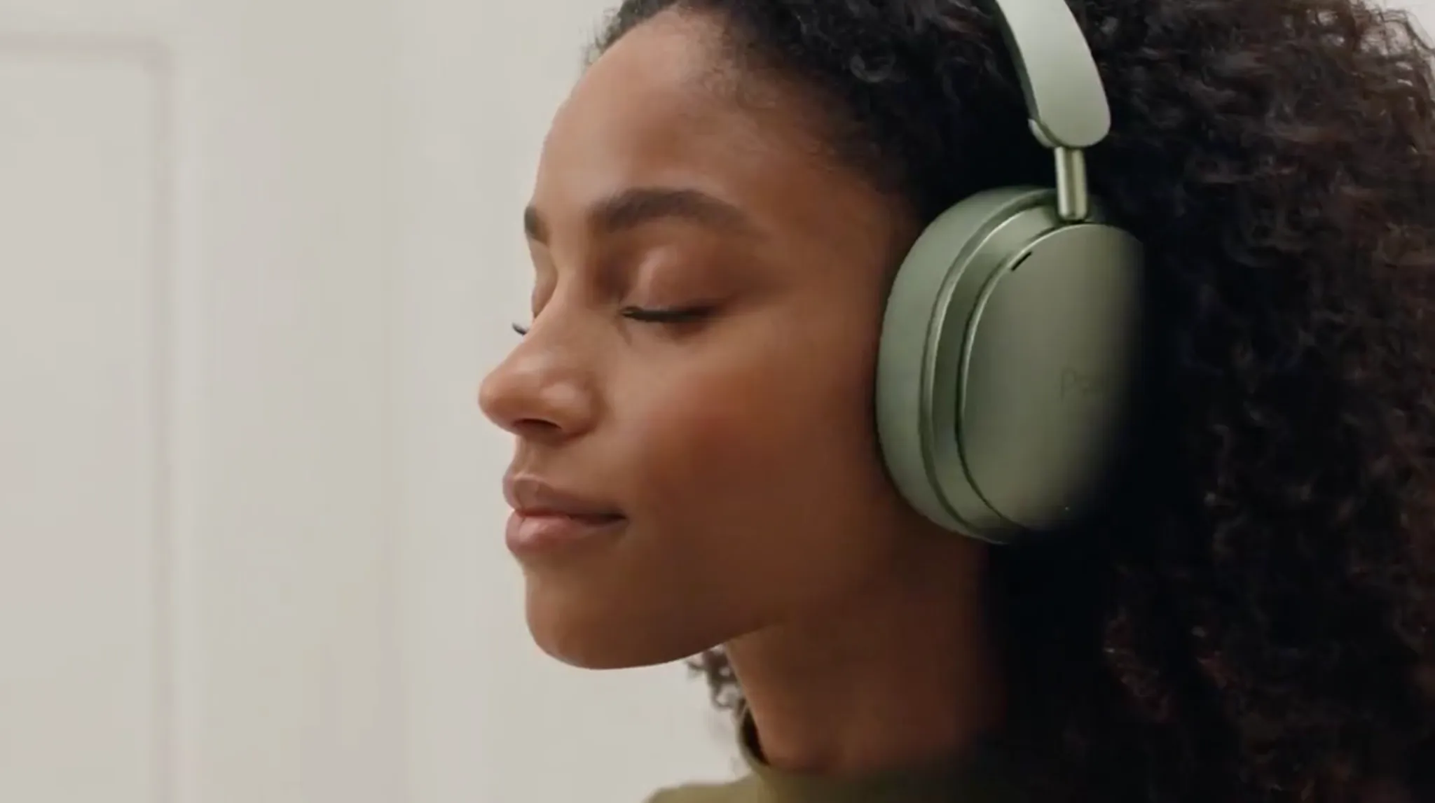 A woman with curly hair relaxes while wearing green headphones.